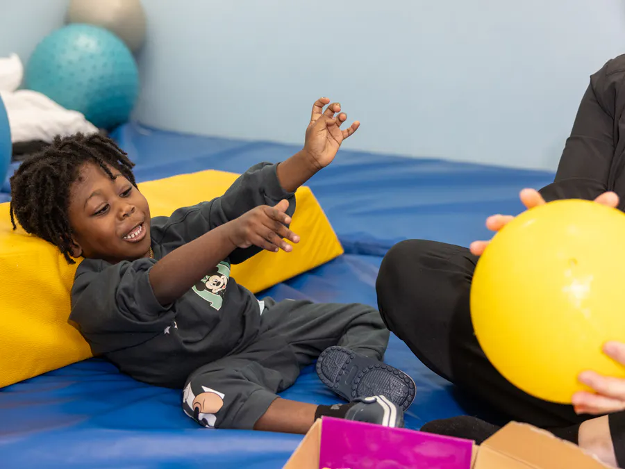 A child laughing and playing catch with a therapist.
