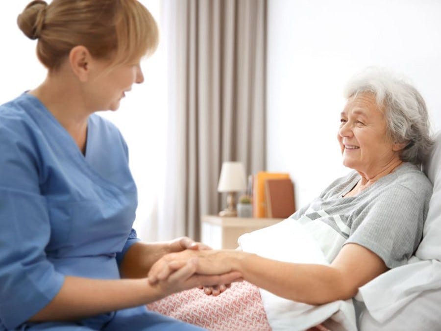 Aid holding woman's hand as she ay in bed