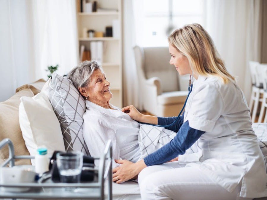 aid helping woman in her bed