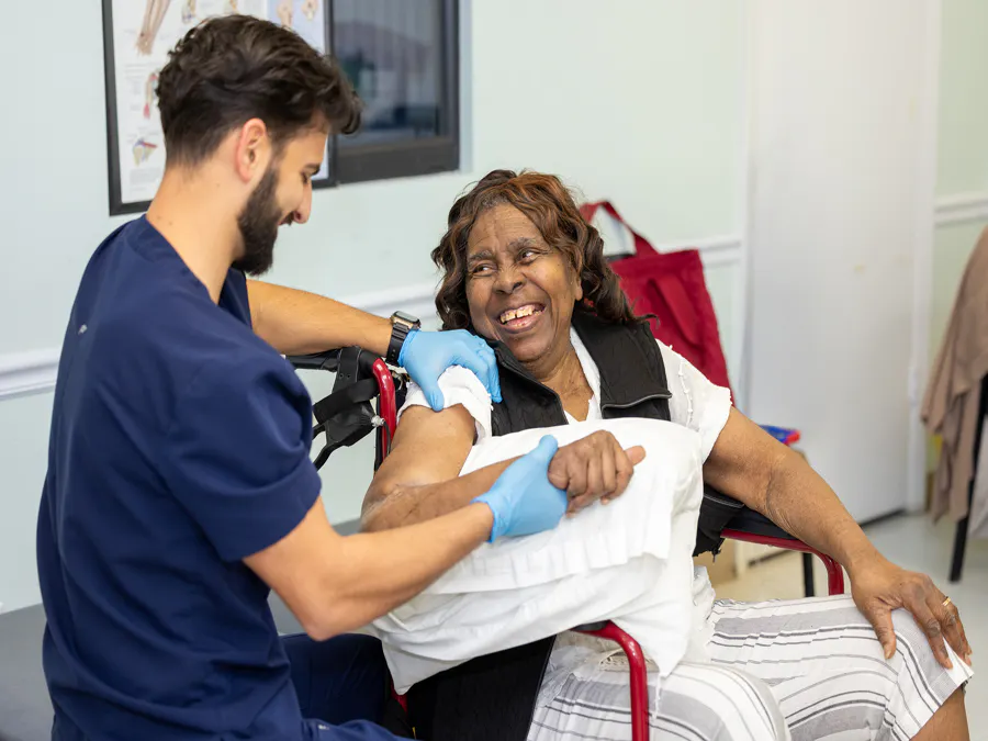 A smiling woman in a wheelchair receiving therapy for her arm.
