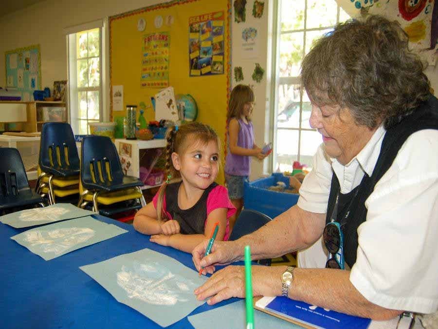Volunteer helping child draw at table